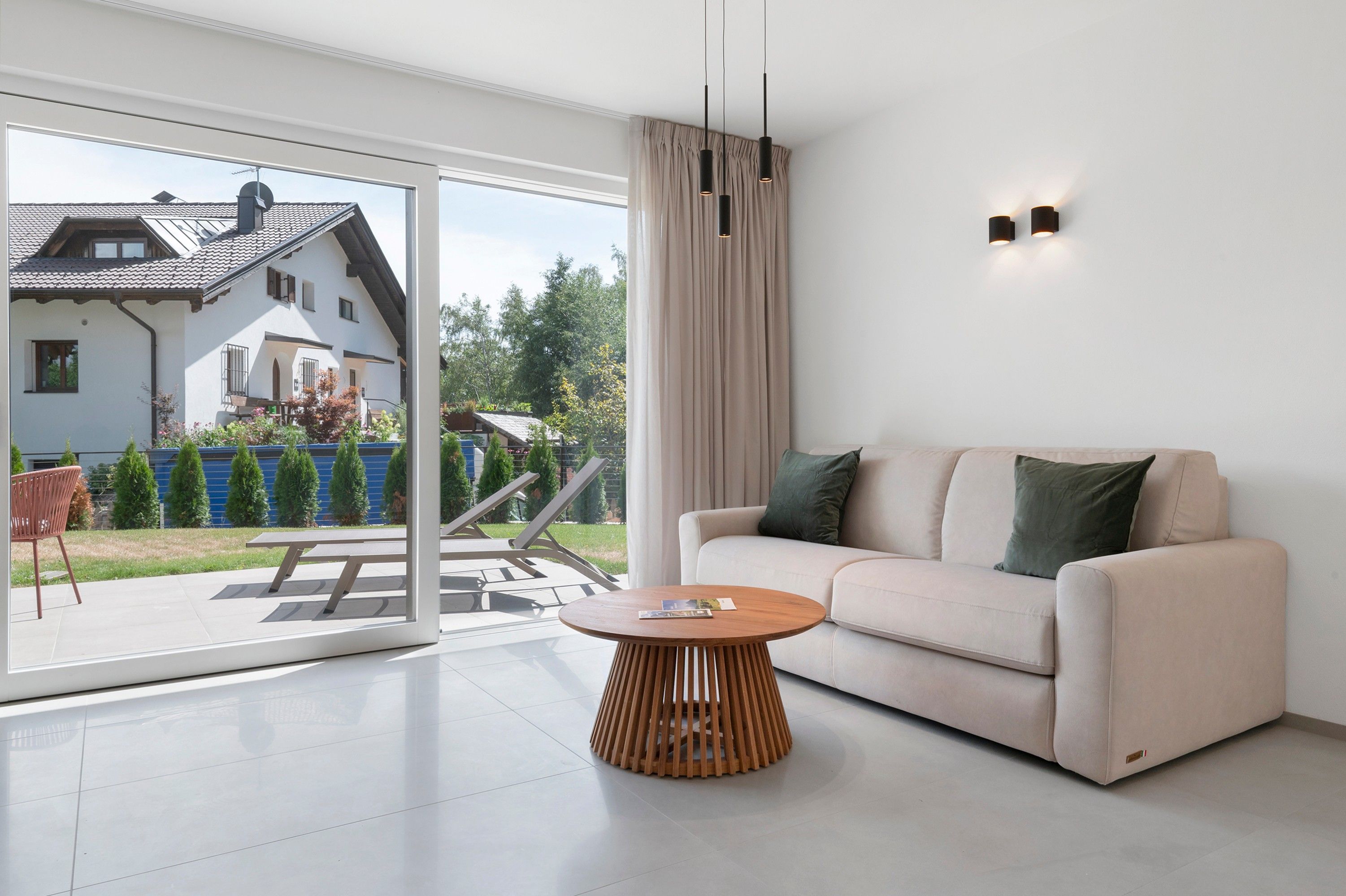 Ein modernes Wohnzimmer mit einer Couch, einem runden Holztisch und einer Schiebeglastür, die auf eine Terrasse führt.