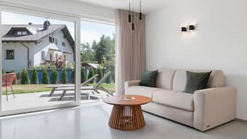 Ein modernes Wohnzimmer mit einer Couch, einem runden Holztisch und einer Schiebeglastür, die auf eine Terrasse führt.