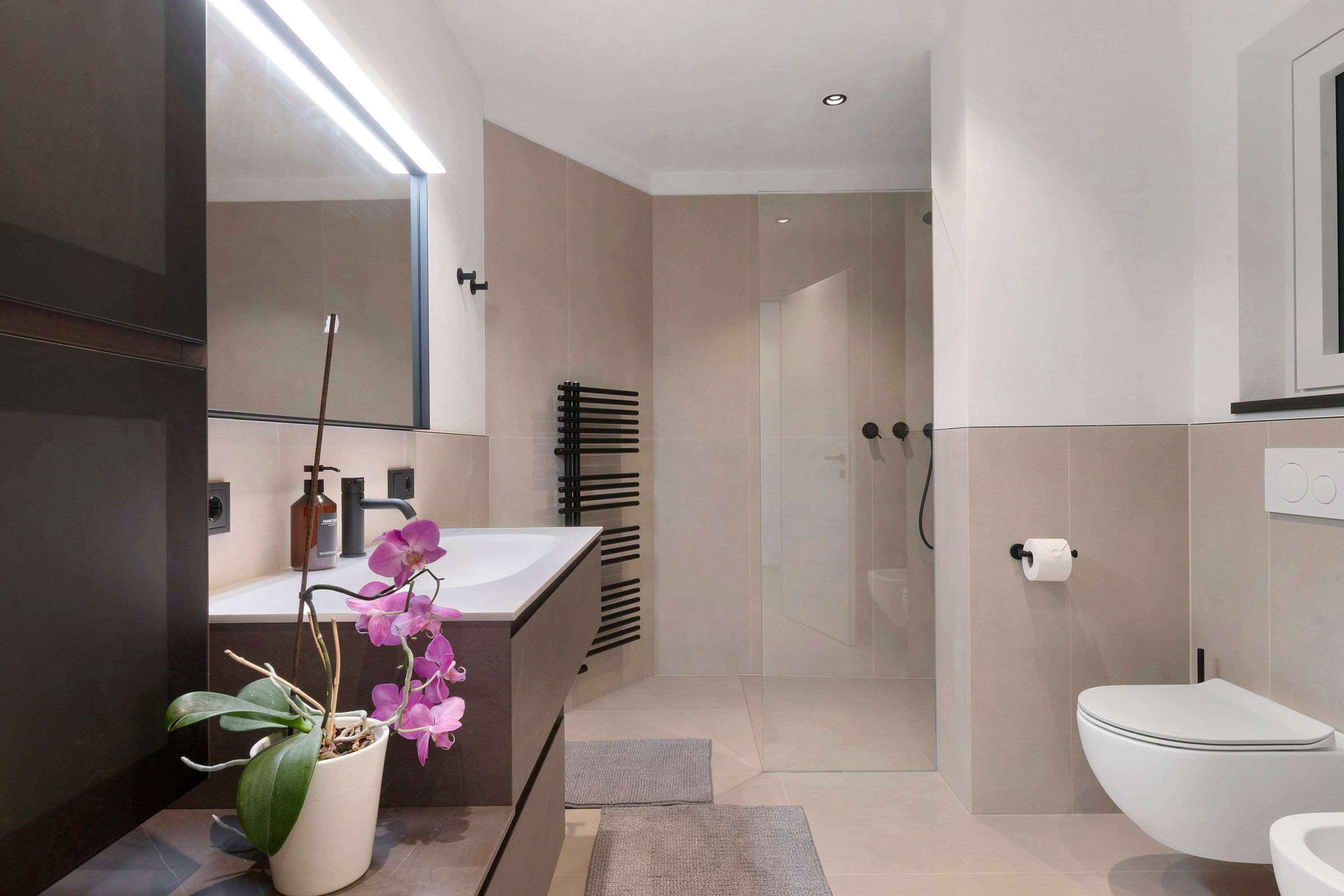 A modern bathroom with a white sink, a mirror, a toilet, and a shower area.
