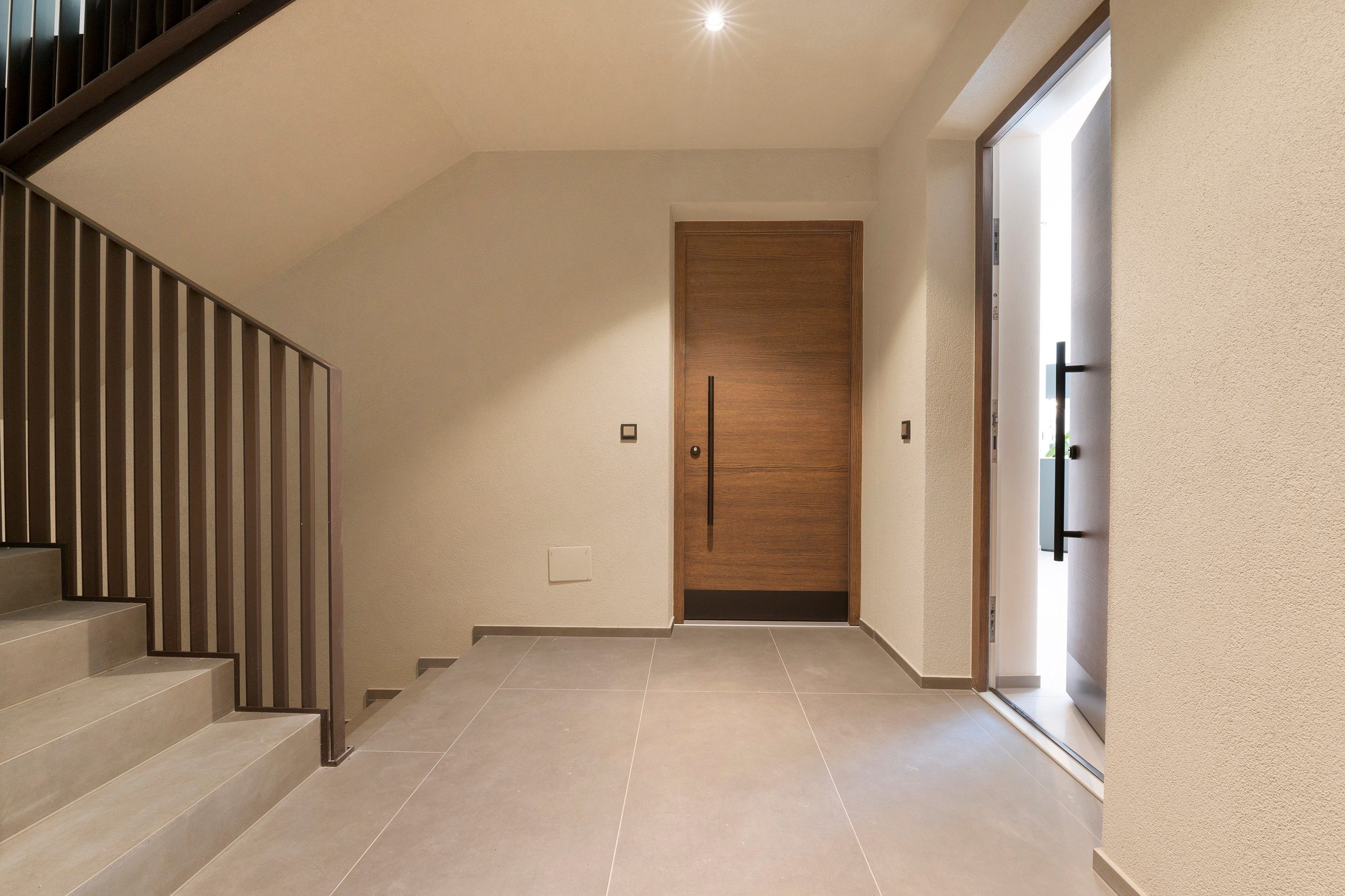 Ein modernes Interieur mit einer Holztür, einer Treppe mit Metallgeländern und einem Fliesenboden.