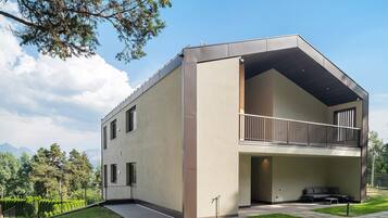 A modern two-story building with a balcony, a flat roof, and a view of mountains in the background.