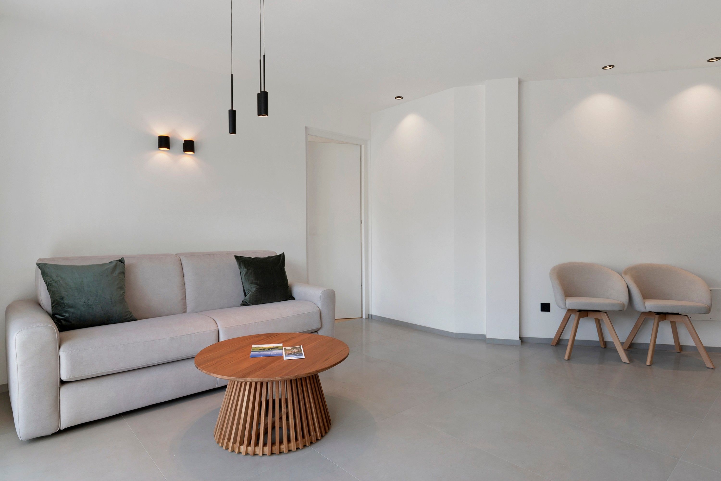 A modern living room with a sofa, two chairs, a coffee table, and pendant lighting.
