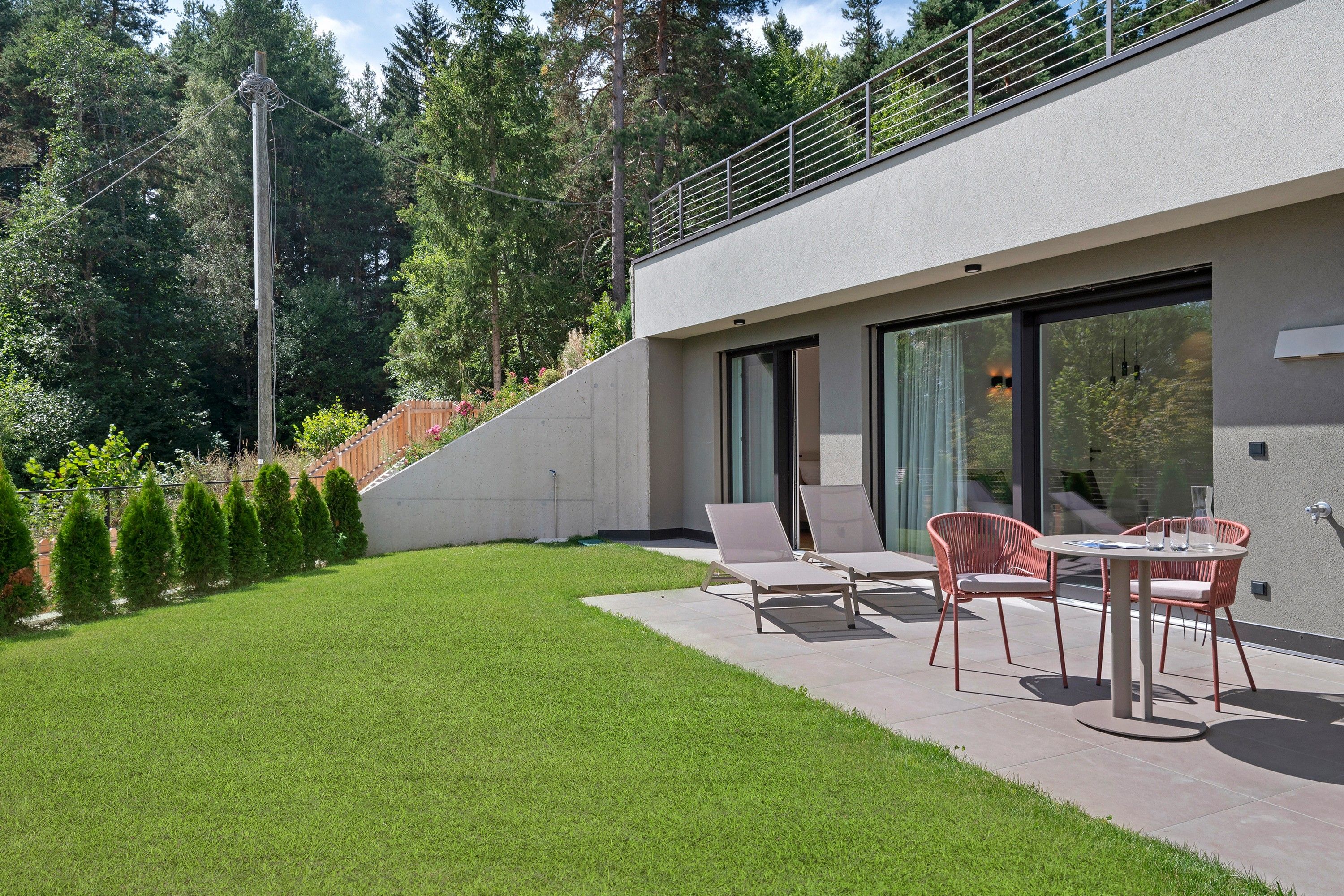 Eine moderne Terrasse im Freien mit Esstisch und Stühlen, umgeben von einem gepflegten Rasen und einem Holzzaun.