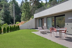 Eine moderne Terrasse im Freien mit Esstisch und Stühlen, umgeben von einem gepflegten Rasen und einem Holzzaun.
