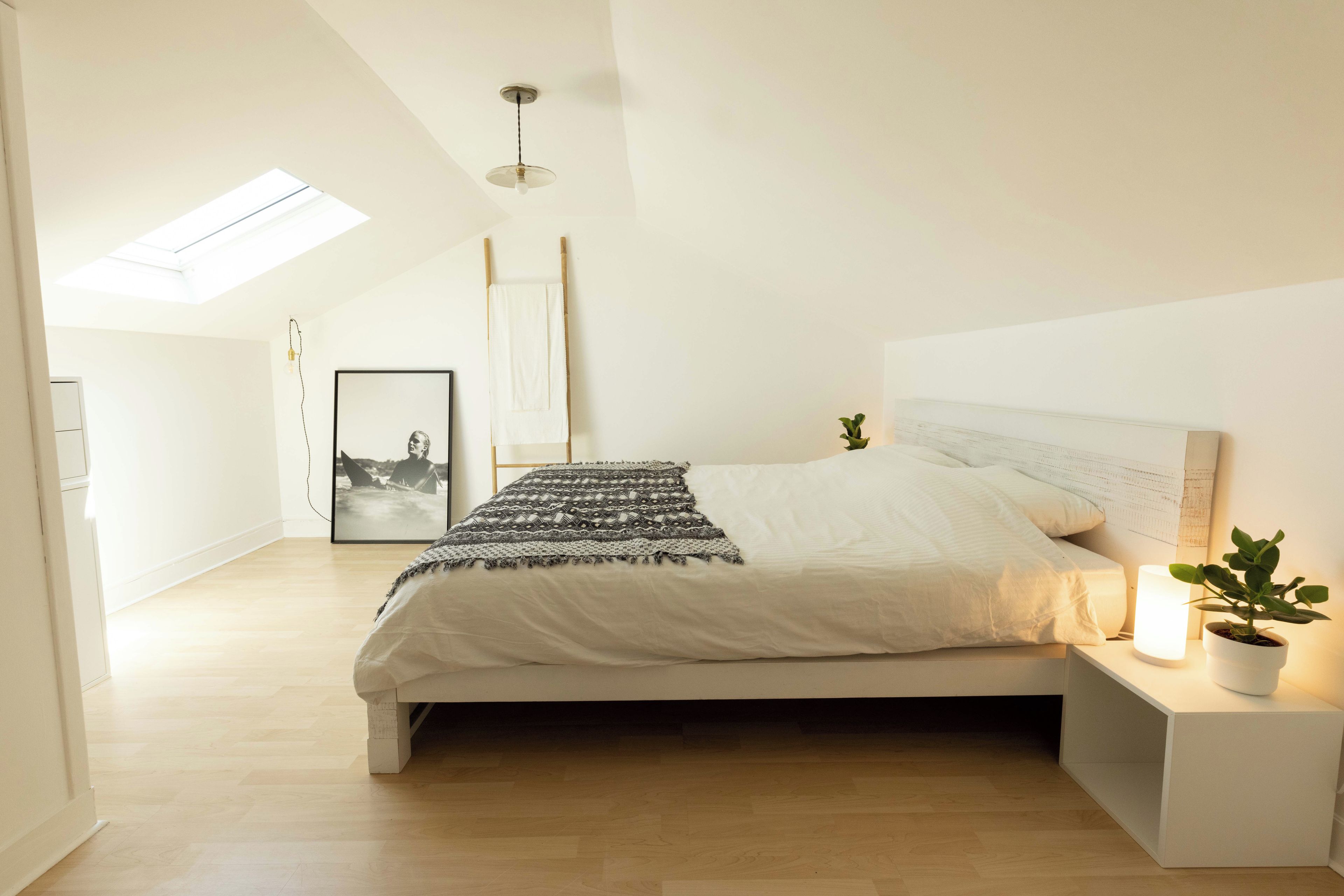 A bedroom with a bed, bedside table, lamp, and a skylight.