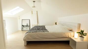 A bedroom with a bed, bedside table, lamp, and a skylight.
