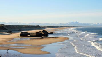 A beach with large rocks, a sandy shore, and a view of distant mountains.