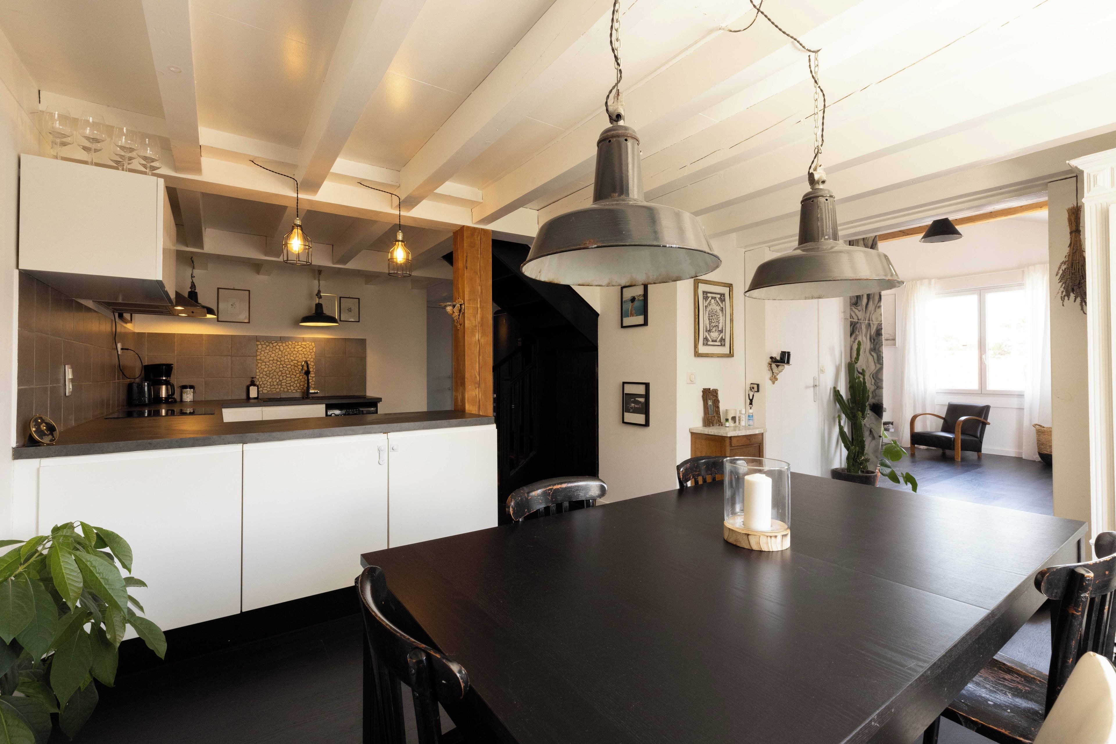 A modern kitchen with white cabinets, a dark wooden dining table, and pendant lighting.