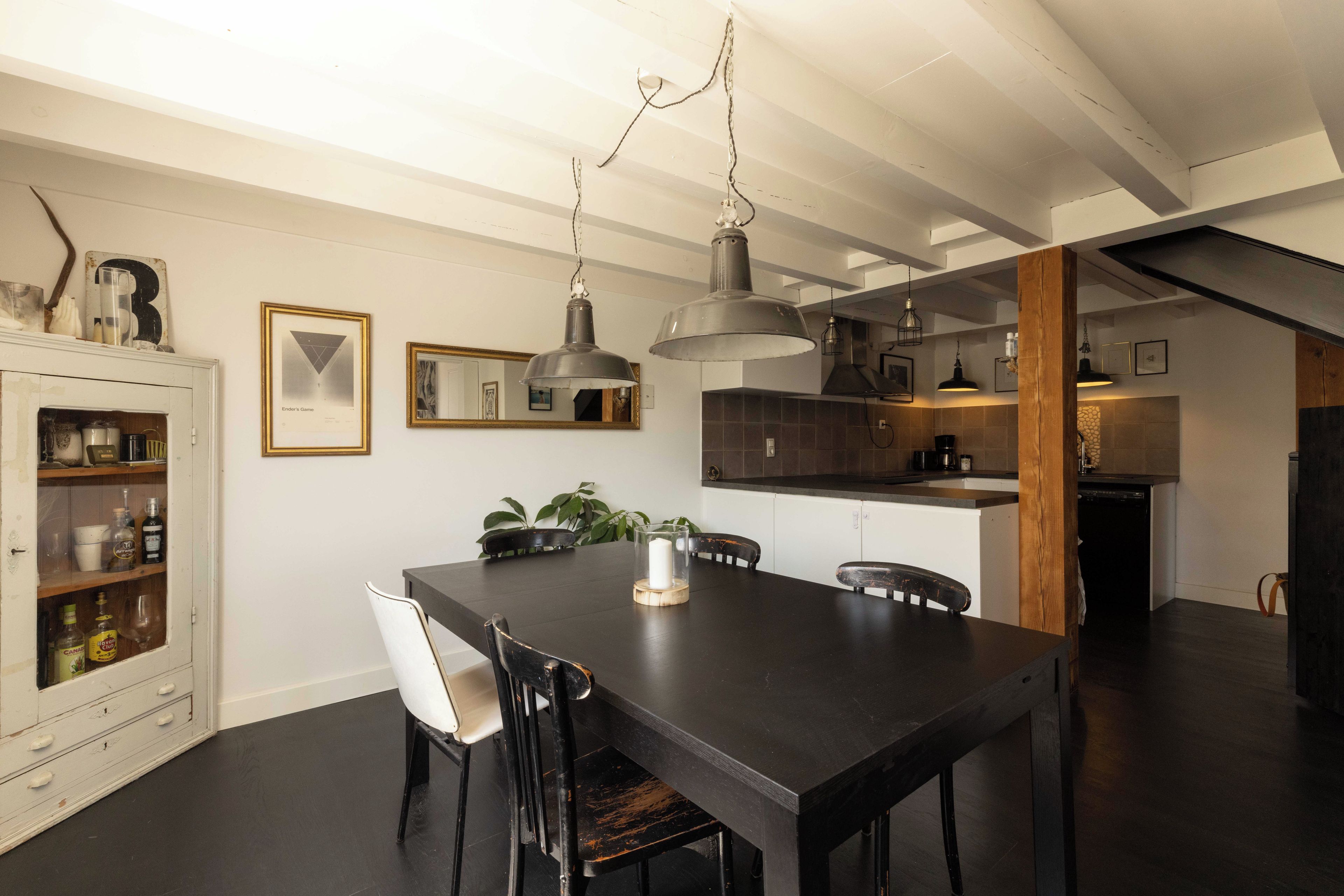 Un espace repas avec une table en bois foncé, des chaises blanches et des luminaires suspendus.