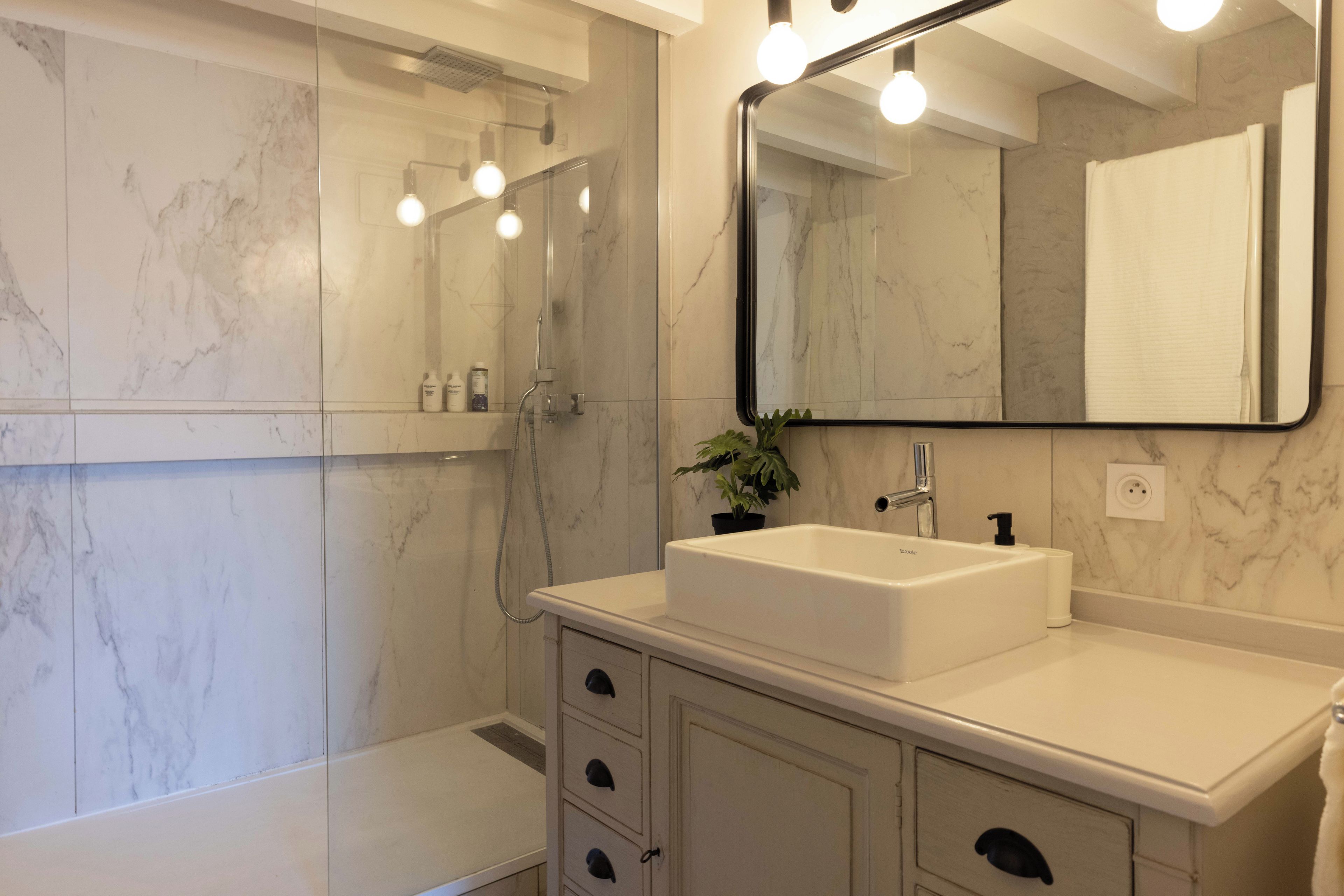 Une salle de bain avec un lavabo blanc, un miroir et une douche.