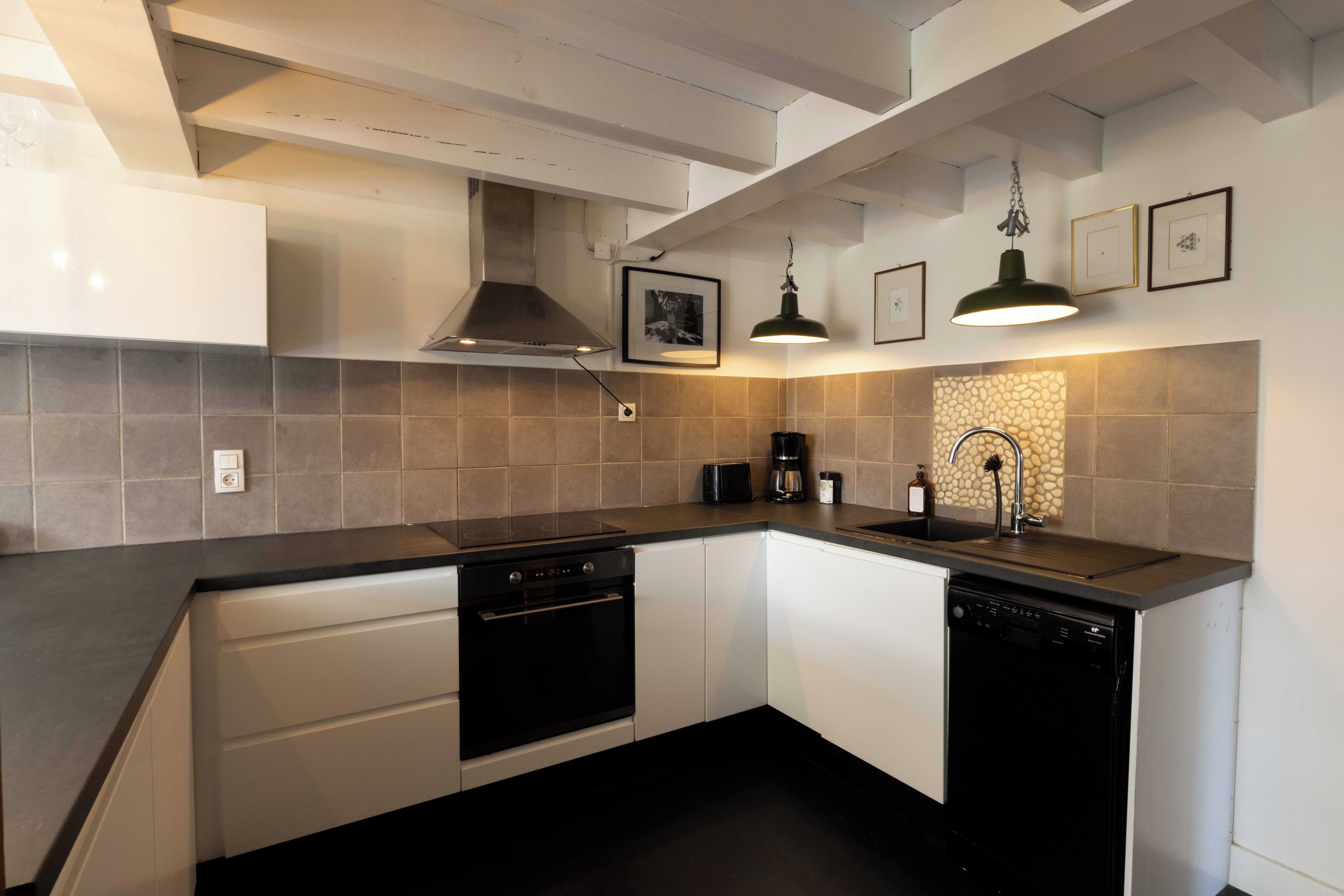 A modern kitchen with white cabinets, a black countertop, a stove, a dishwasher, a coffee maker, and a sink with a faucet.