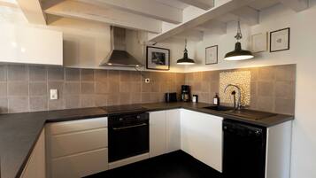 A modern kitchen with white cabinets, a black countertop, a stove, a dishwasher, a coffee maker, and a sink with a faucet.