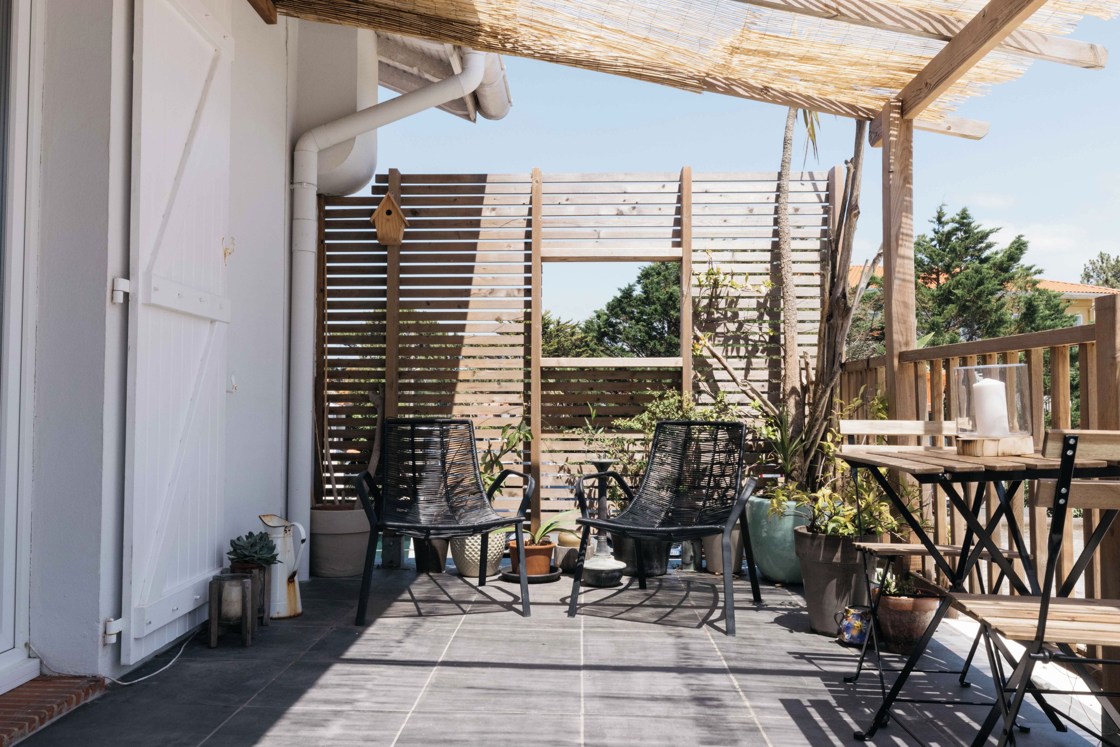 Un patio al aire libre con dos sillas de metal negro, una mesa de madera y plantas en macetas.