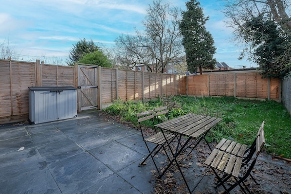Un jardin avec une clôture en bois, un abri en métal et une table de pique-nique avec des bancs.