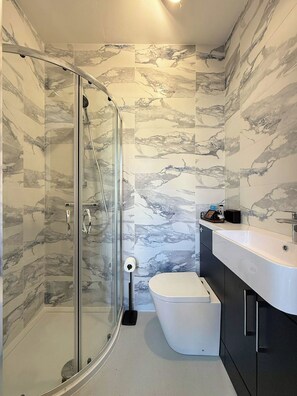 A modern bathroom with a glass shower enclosure, a toilet, and a sink area. - Beautiful 1-Bedroom City Retreat (Sheffield)