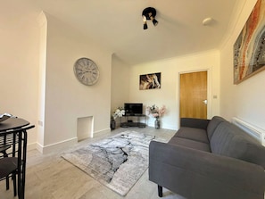 A living room with a grey sofa, a black coffee table, a TV, and a clock on the wall. - Beautiful 1-Bedroom City Retreat (Sheffield)