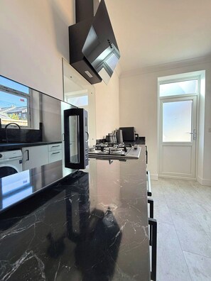 A modern kitchen with a black marble countertop, a built-in oven, and a window overlooking a street. - Beautiful 1-Bedroom City Retreat (Sheffield)