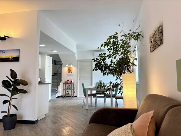 Una sala de estar moderna con un sofá marrón, una planta en maceta y una zona de comedor con mesa y sillas.