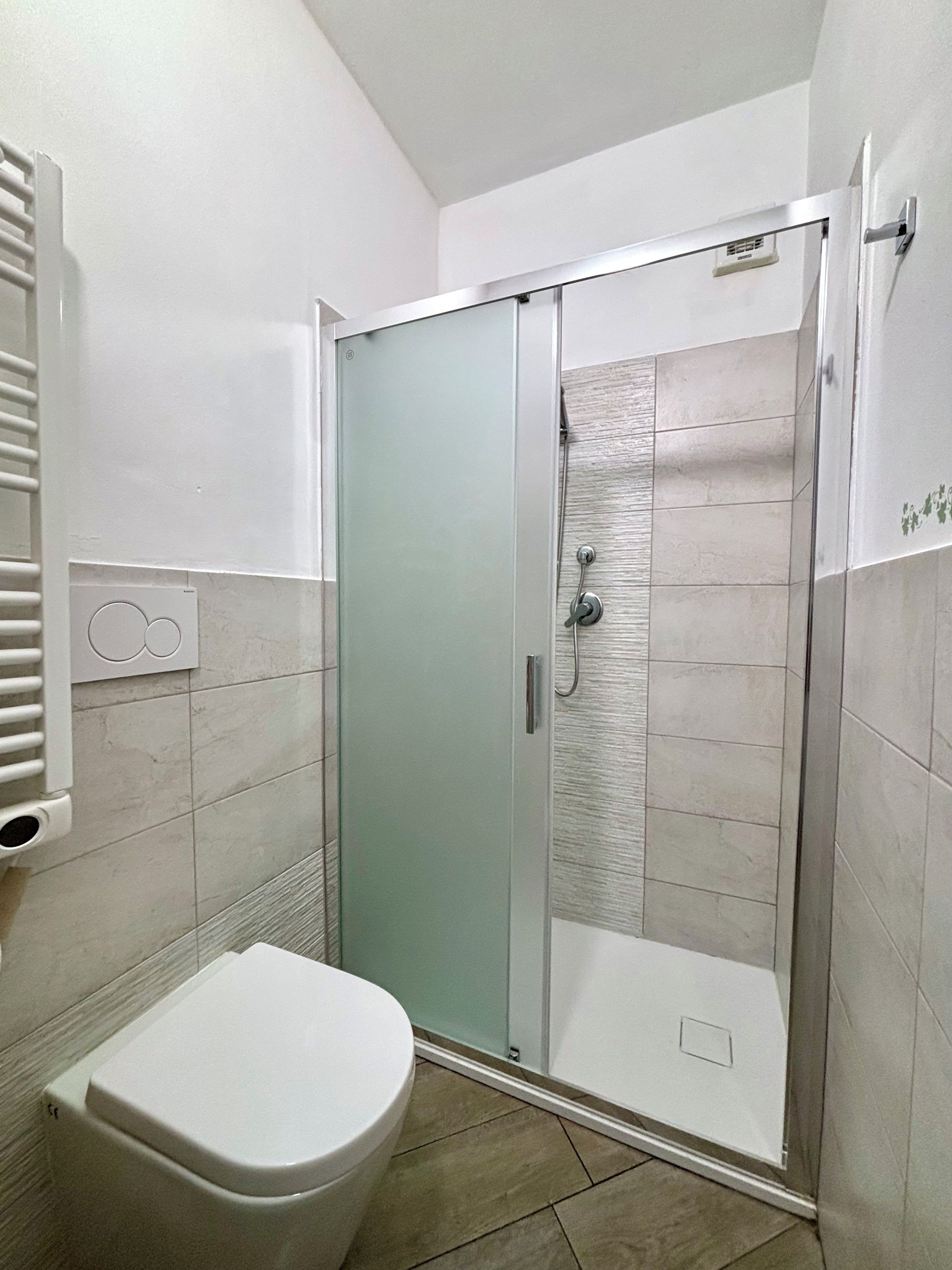 Un bagno con doccia in vetro, un water e un appendi asciugamani.