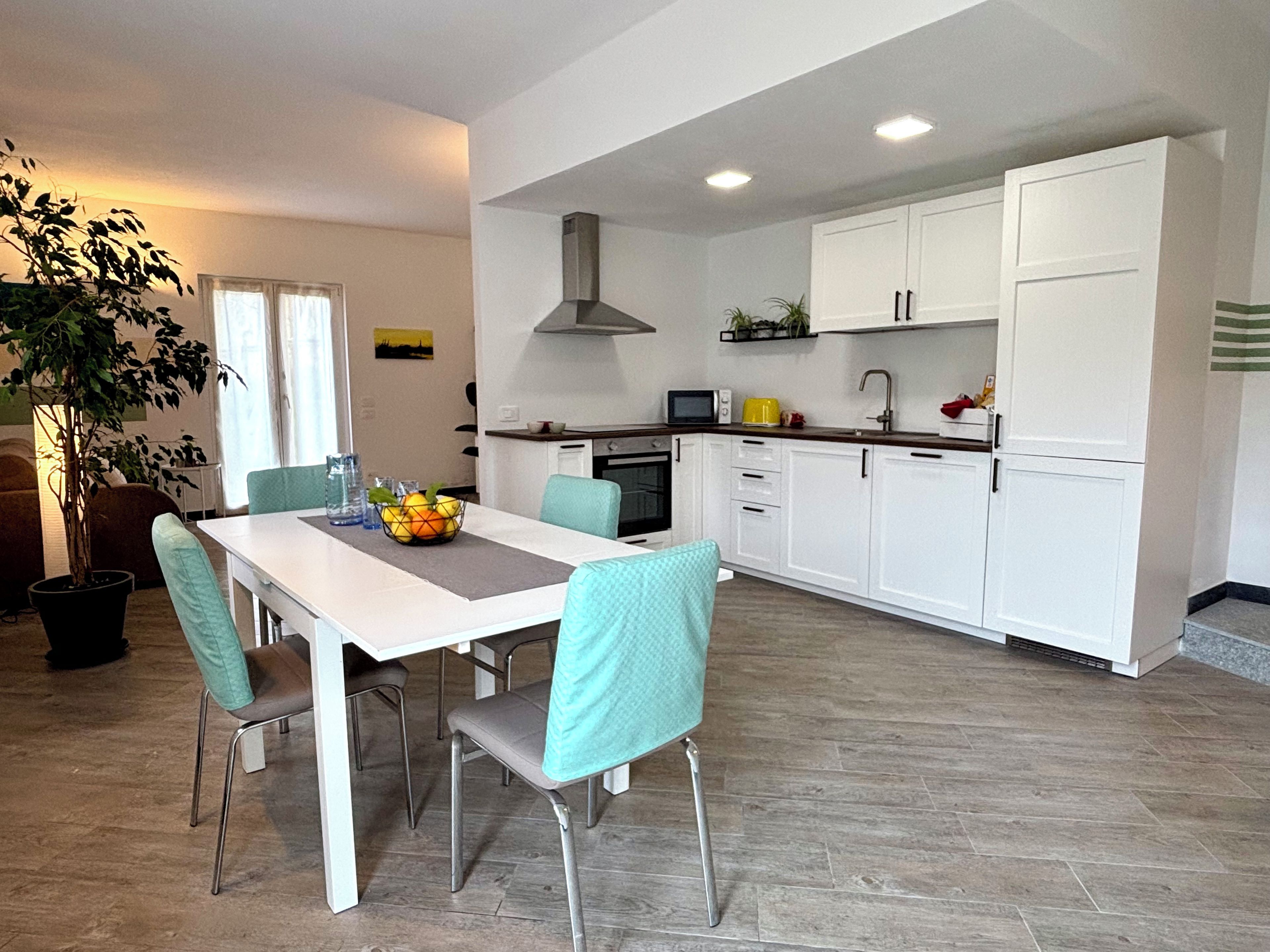 Une cuisine moderne avec des meubles blancs, une table à manger avec des chaises et une plante en pot.