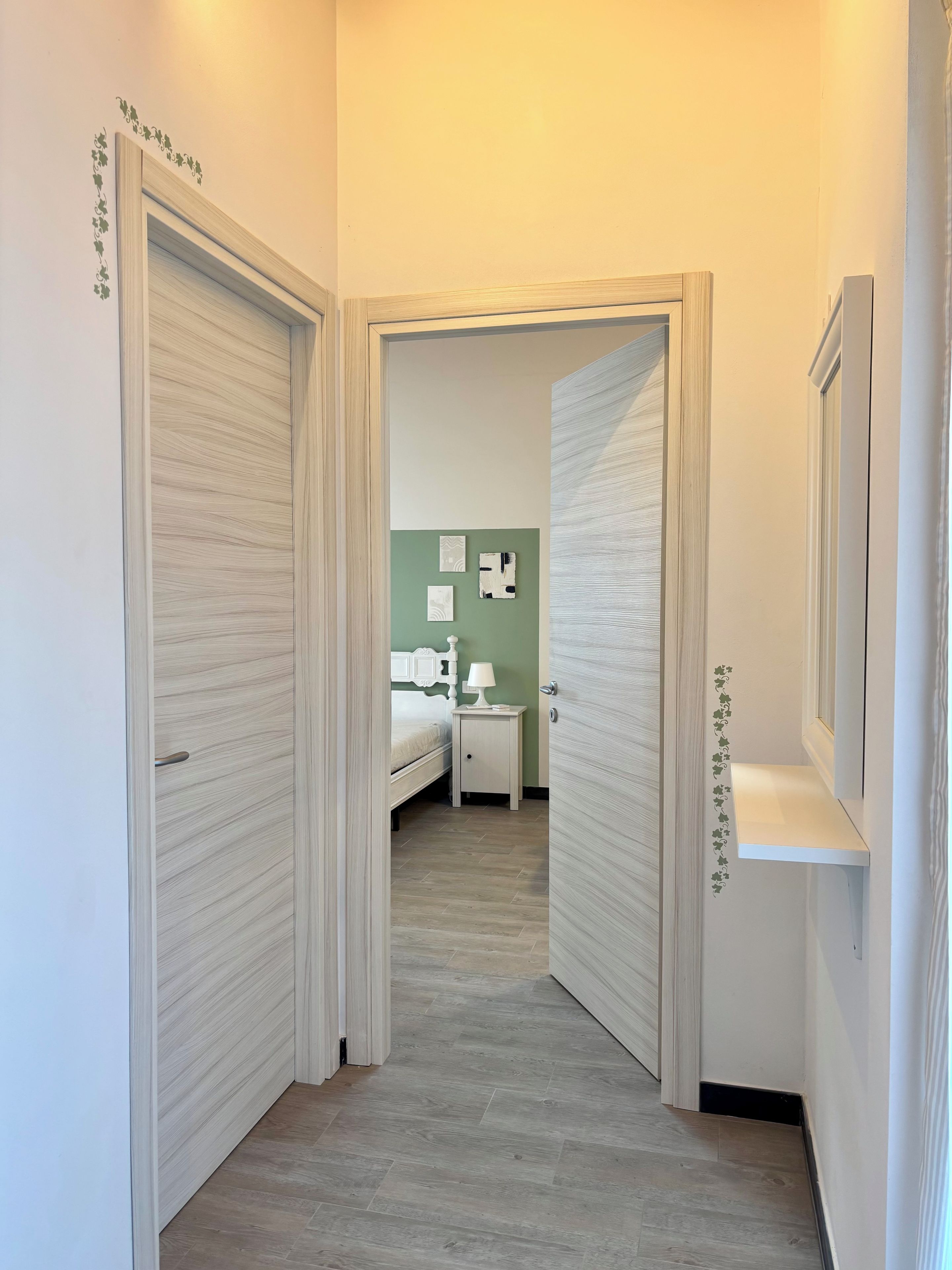 Un couloir mène à une chambre à coucher qui contient un lit, une table de chevet et une lampe fixée au mur.