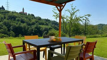 Ein Essbereich im Freien mit Tisch und Stühlen, einem Blumentopf und Blick auf einen Hügel mit einem Turm.