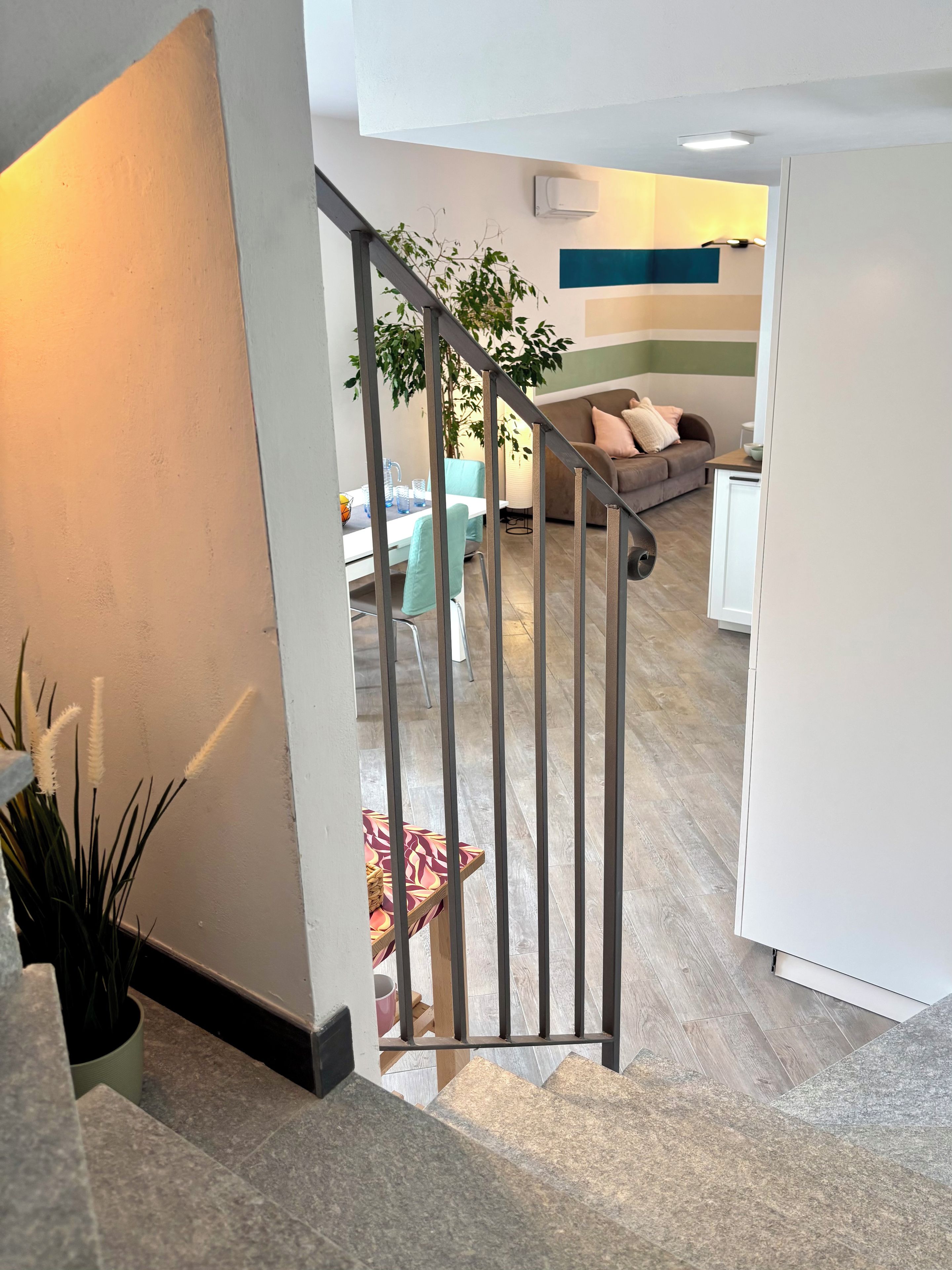 Eine Treppe führt zu einem Wohnbereich mit einer Couch, einem Esstisch und einer Topfpflanze.