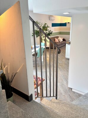 Un escalier menant à un espace de vie comprenant un canapé, une table à manger et une plante en pot.