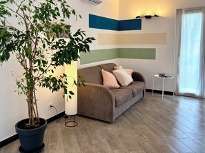 Un salon avec un canapé marron, une petite table ronde, une plante en pot et un mur orné d’œuvres d’art abstraites.