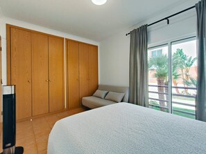 A bedroom with a bed, a sofa, a wardrobe, and a sliding glass door to a balcony. - Apartment 'Quinta Da Gomeira 68' with shared pool, Wi-Fi and air conditioning (Tavira)