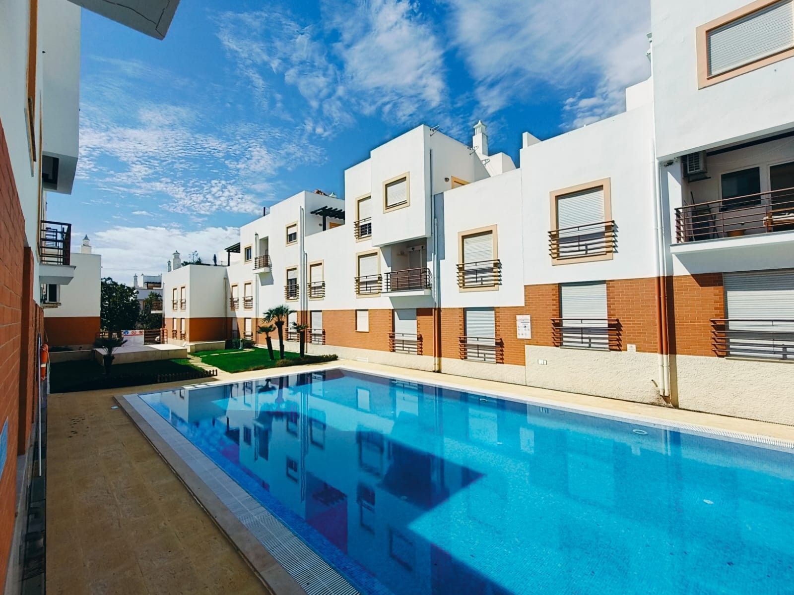 Un moderno edificio de apartamentos con piscina, balcones y un cielo azul despejado.