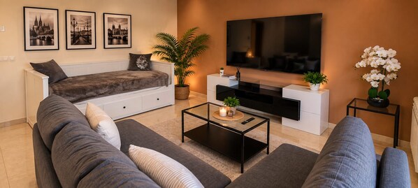 A modern living room with a sofa, a coffee table, a flat-screen TV, and decorative plants.