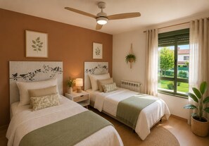 A bedroom with two beds, a ceiling fan, a window with curtains, and a view of greenery outside.