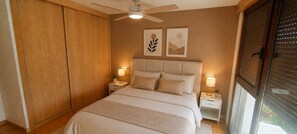 A bedroom with a bed, nightstands, a ceiling fan, and artwork on the wall.