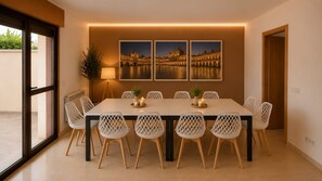 A dining area with a long table, white chairs, and three framed pictures on the wall.
