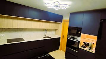 Une cuisine moderne avec des meubles de couleur sombre, un plan de travail en marbre, un four encastré et un ventilateur de plafond.