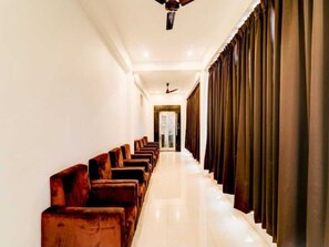 A hotel corridor with rows of wooden chairs and a ceiling fan. - Deluxe The Silver Tree (Lucknow)