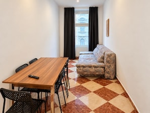 Ein Zimmer mit Esstisch, Stühlen, einer Couch und Blick auf ein Gebäude durch ein blickdichtes Fenster.