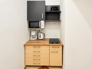 Eine Küchenzeile mit Mikrowelle, Kaffeemaschine, Wasserkocher und einer schwarzen Induktionskochplatte.