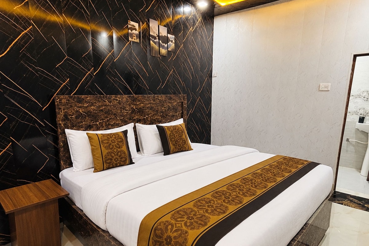 A hotel room with a large bed, a wooden nightstand, and a bathroom visible through an open door.