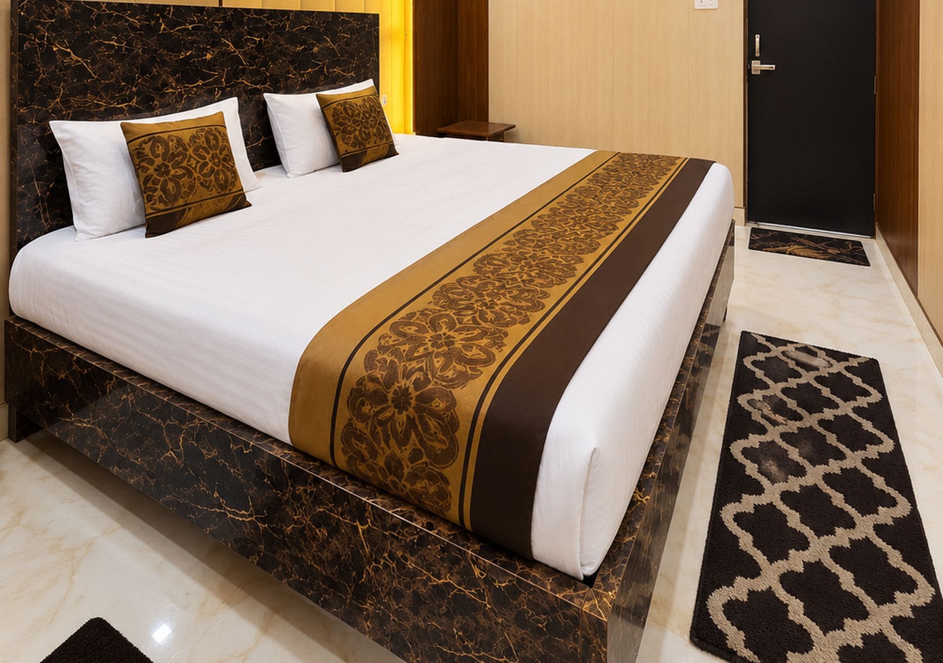 A hotel room with a large bed, a marble bedside table, a wooden door, and a patterned rug.