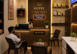A hotel reception area with a reception desk, a computer, and a sign indicating the check-out time. - Hotel Utsav Kunj (Sitapur)