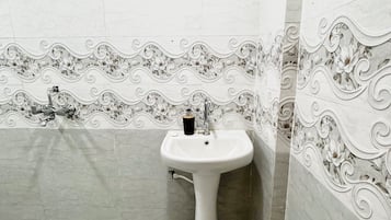 A bathroom with a white pedestal sink, a mirror, and decorative floral tiles on the walls.