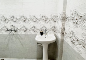 Un baño con un lavamanos pedestal blanco, un espejo y azulejos decorativos con motivos florales en las paredes.