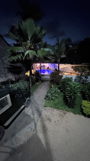 A pathway leading to a pool area with palm trees and a thatched-roof structure. - Family Luxury suite accommodates 4 guests (Malindi)