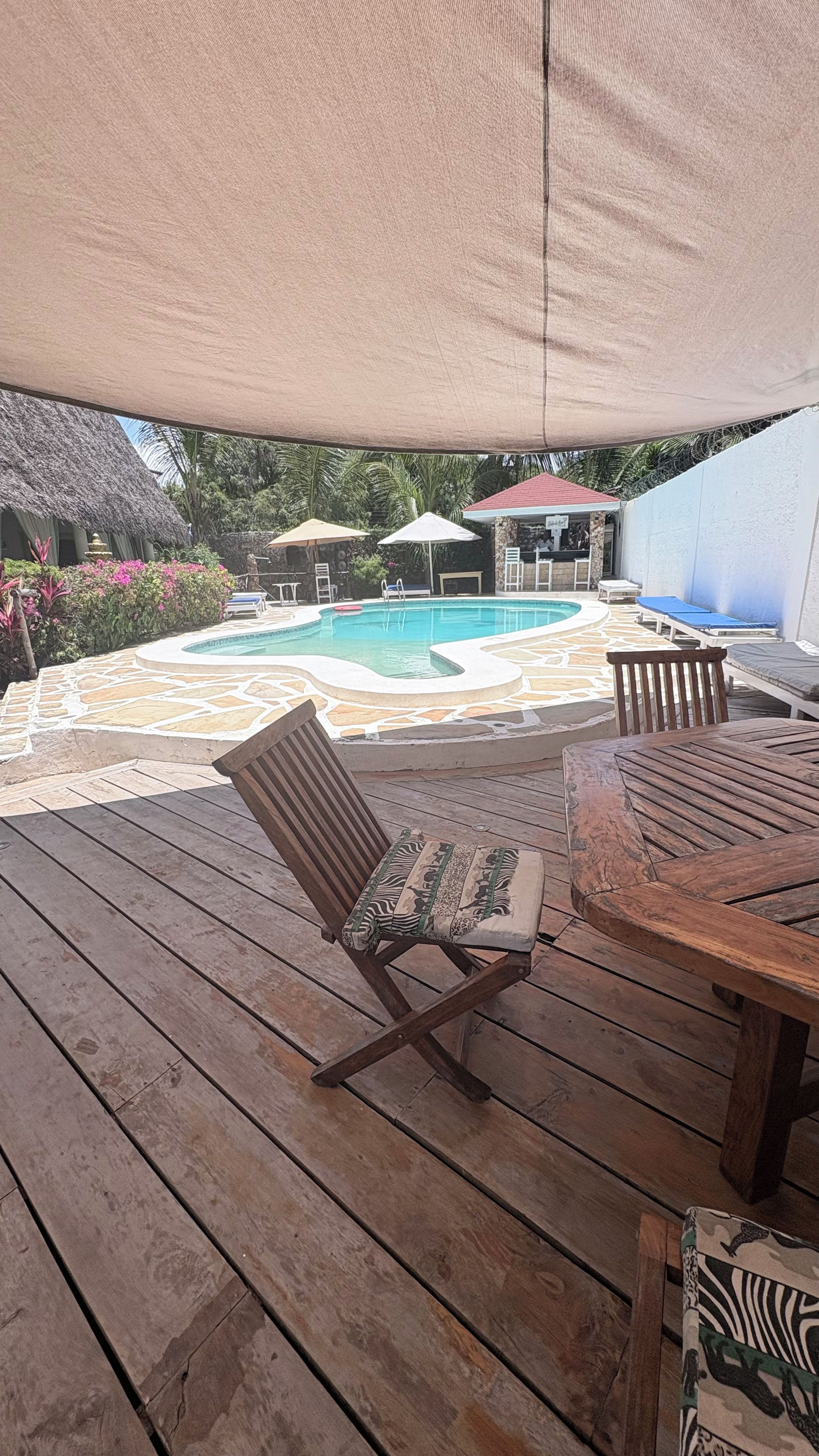 A wooden deck with a pool, lounge chairs, and a thatched-roof structure.