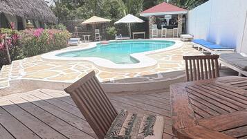 A wooden deck with a pool, lounge chairs, and a thatched-roof structure.