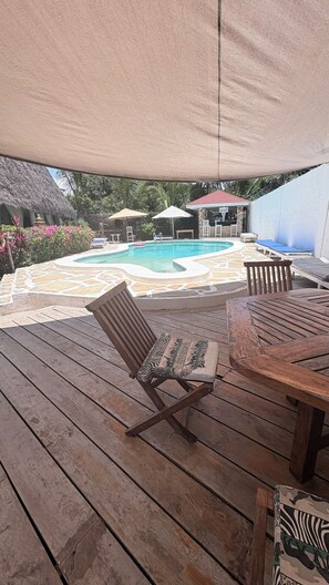 A wooden deck with a pool, lounge chairs, and a thatched-roof structure. - Family Luxury suite accommodates 4 guests (Malindi)