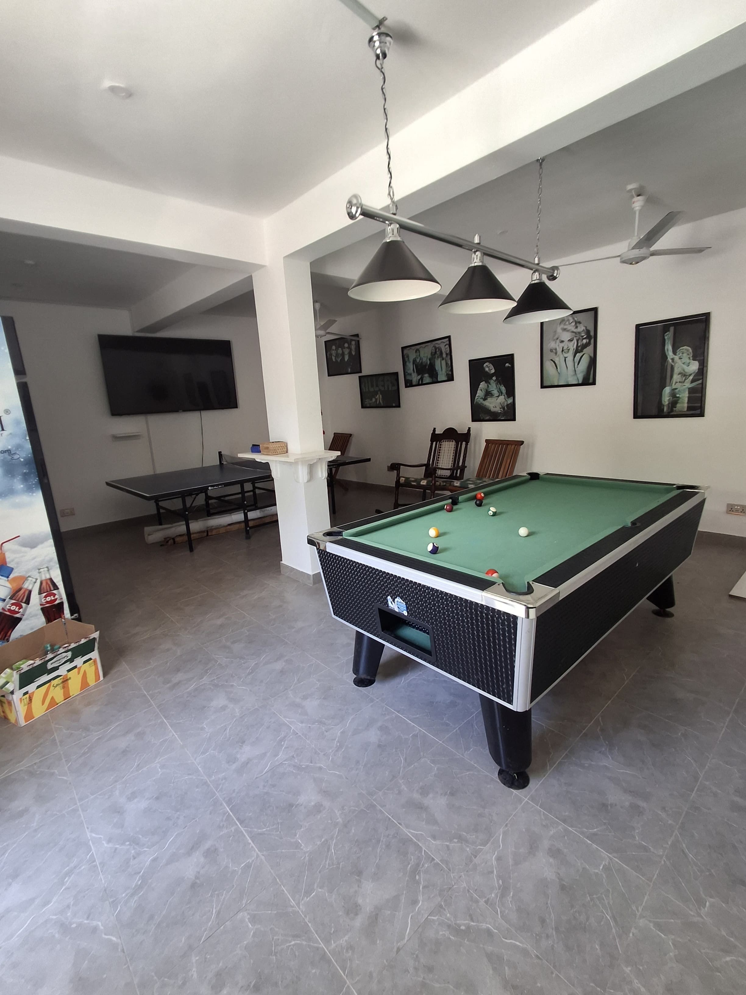 A pool table in a room with a ceiling fan, a television mounted on the wall, and framed pictures.