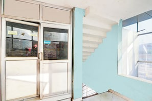 Una habitación con una pared parcialmente dañada, una puerta con paneles de vidrio y una ventana con vista al exterior.